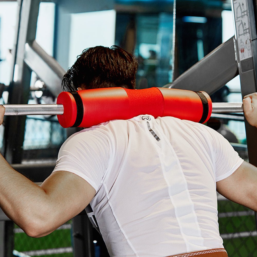 Foam barbell squat pad for weightlifting shoulder support shown in red and being used by a person to demonstrate its fit over the shoulders during a squat position.