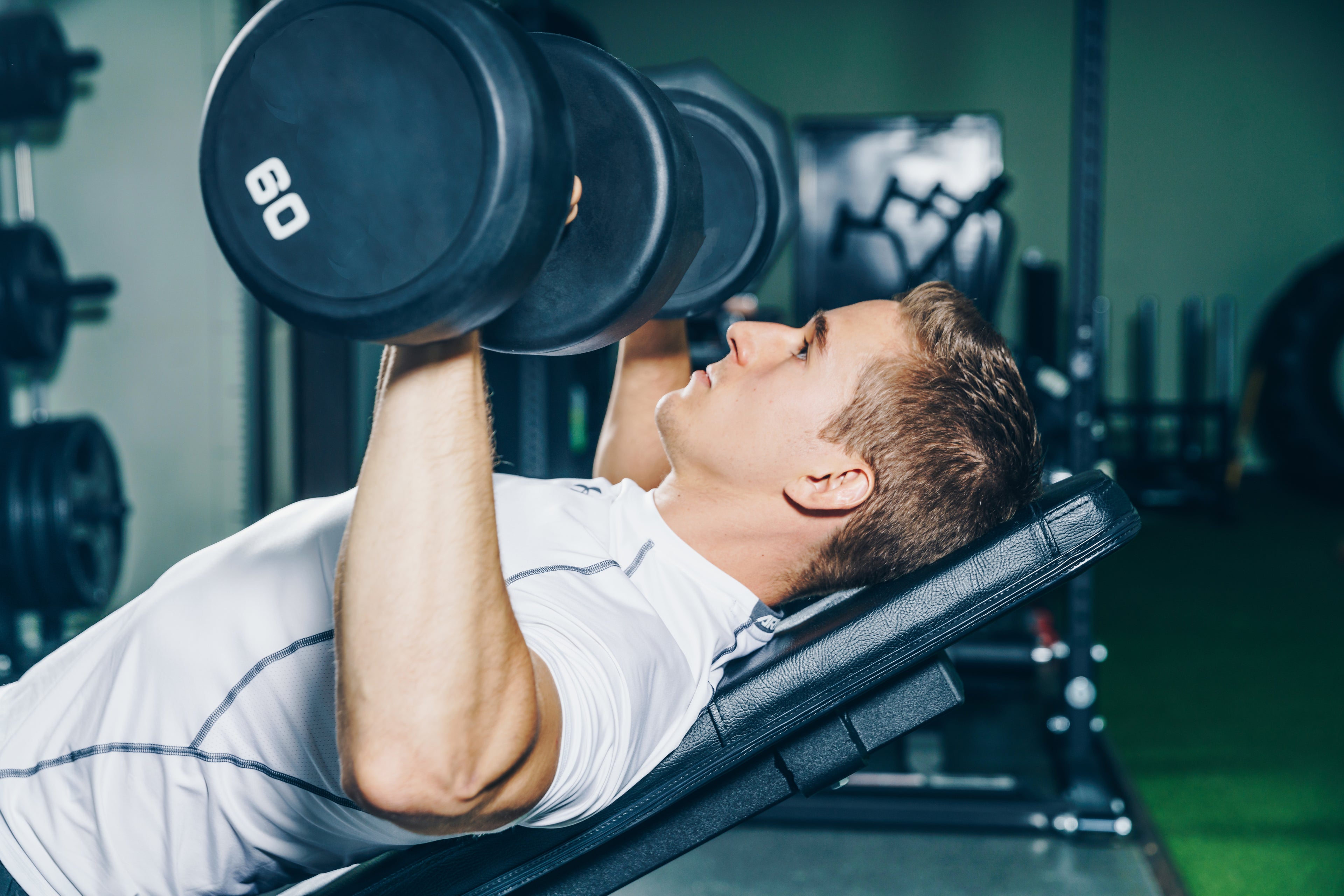 A man in a fitness T-shirt performing a dumbbell incline press on a bench, highlighting strength, focus, and commitment to men's fitness - TNT Fitness Gear