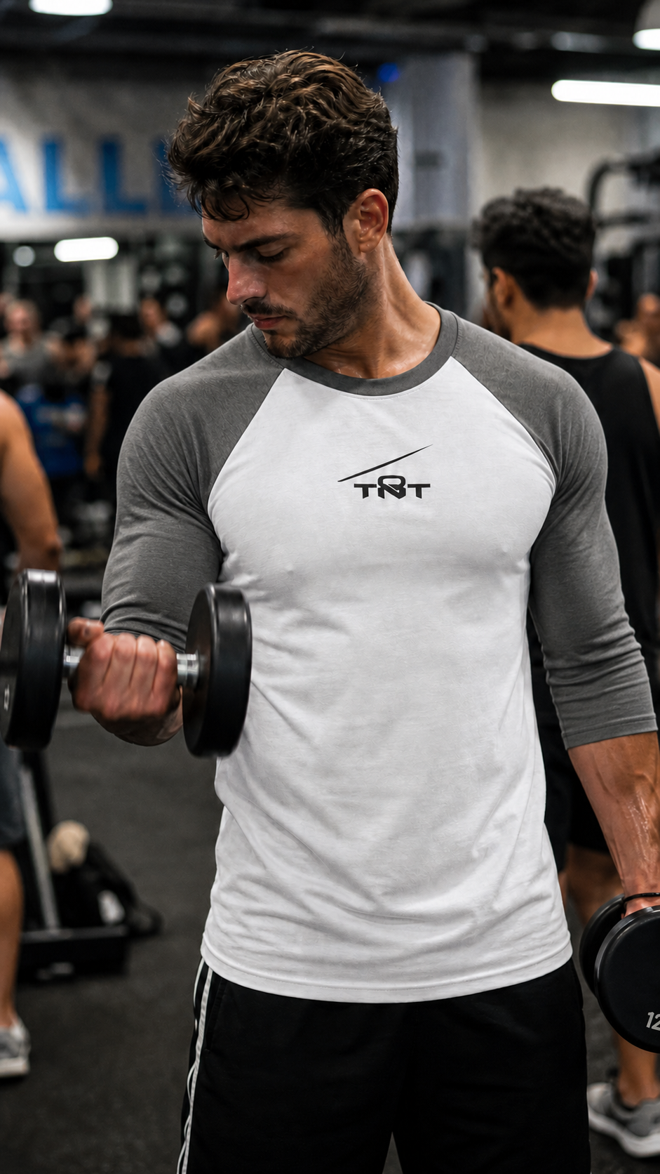 Man lifting weights in a gym wearing a Gray and white TNT Performance Raglan Training Shirt with 3/4 sleeves and black TNT tension line logo.
