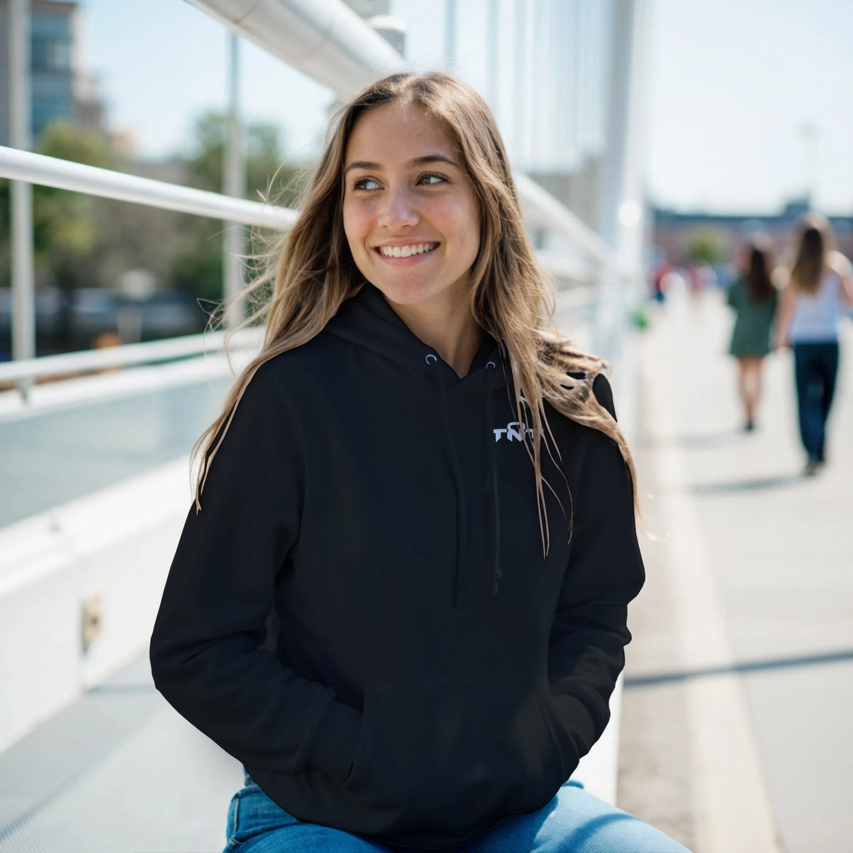 Female model wearing black TNT Fitness Gear unisex training hoodie in a casual lifestyle setting.
